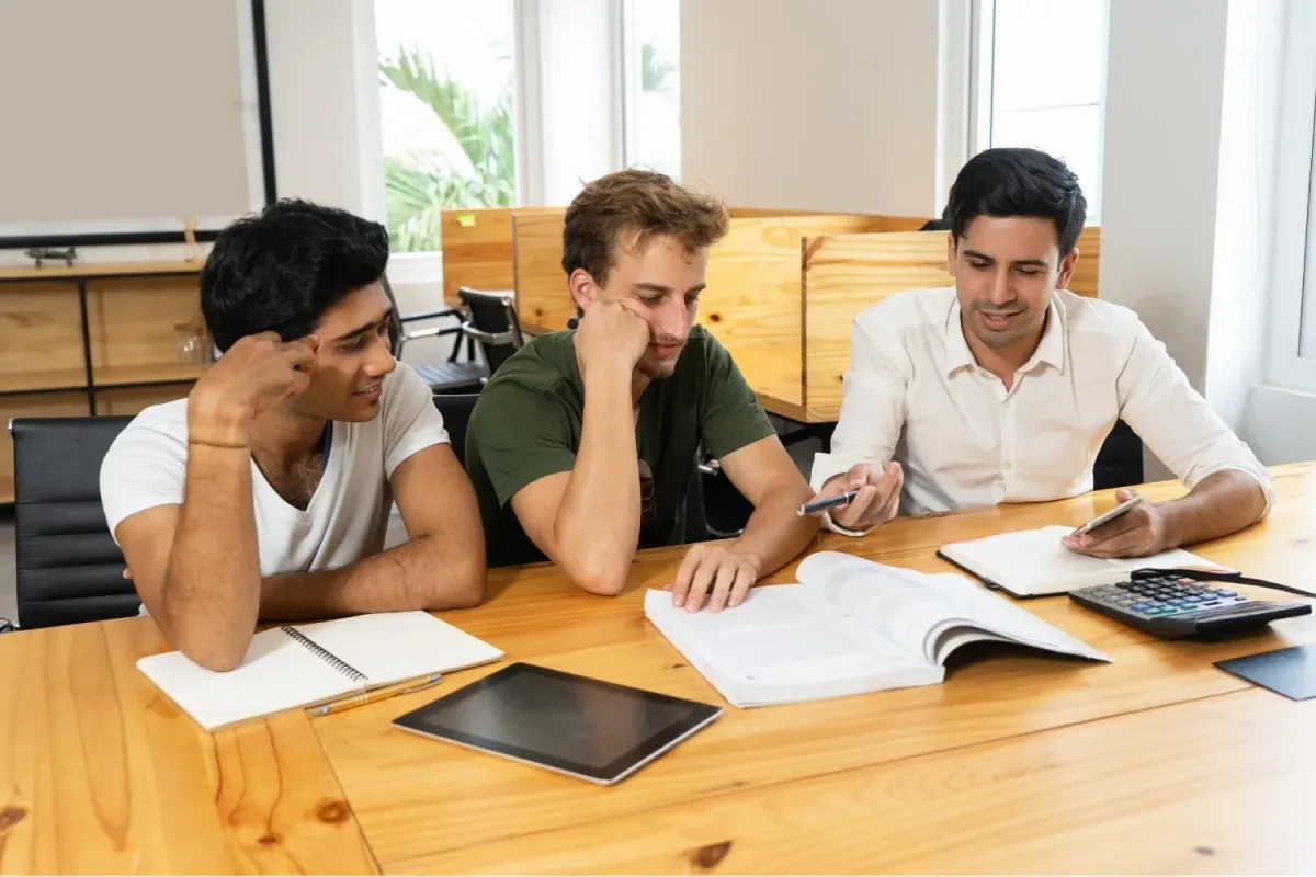 Three students studying together at a table with books and a calculator